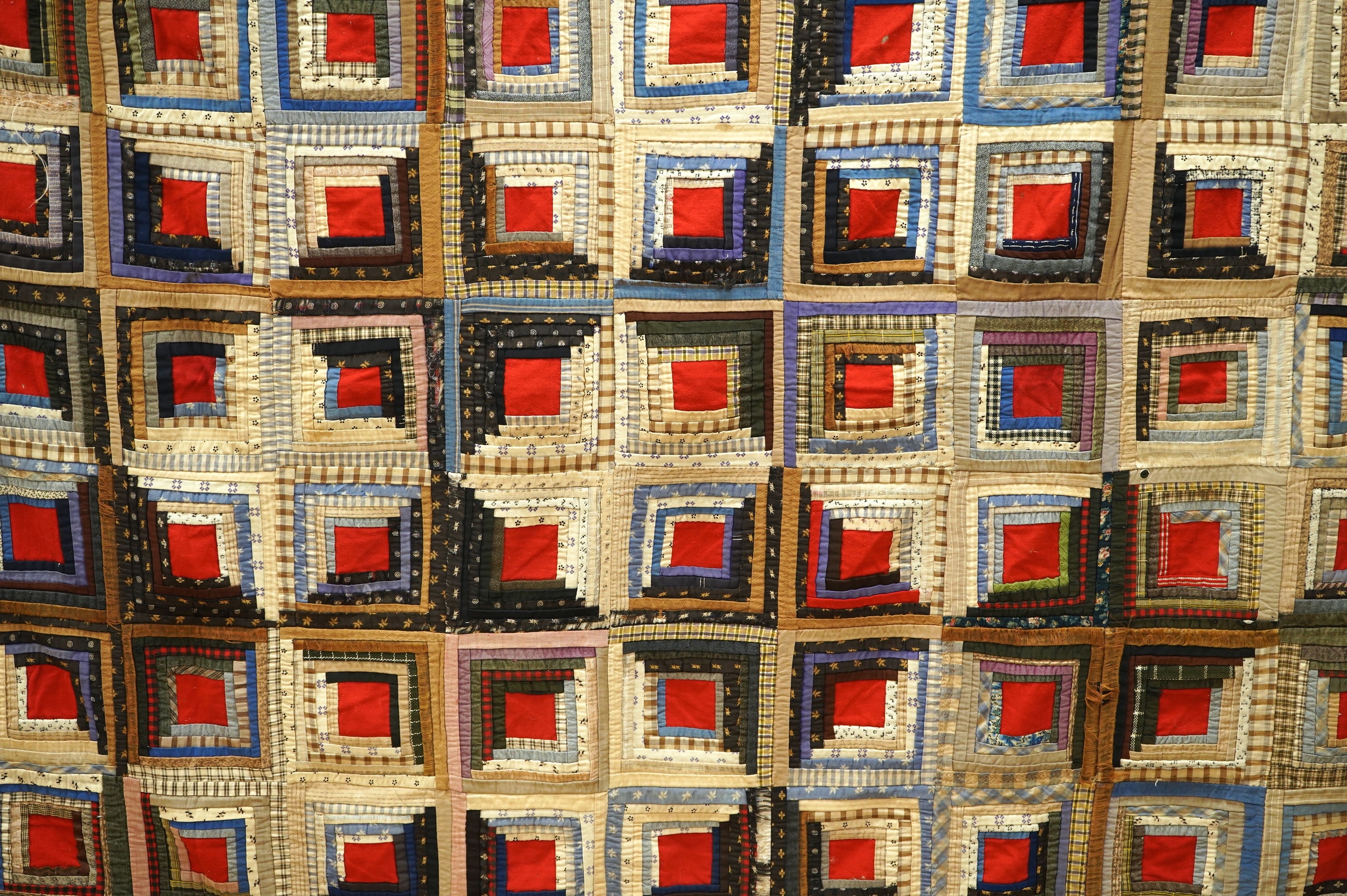 An early 20th century American ‘Log Cabin’ quilt, with a simple same coloured squared patchwork under side, the ‘Log Cabin’ worked in narrow bands of multi patterned and coloured strips of fabric into squares with a plai